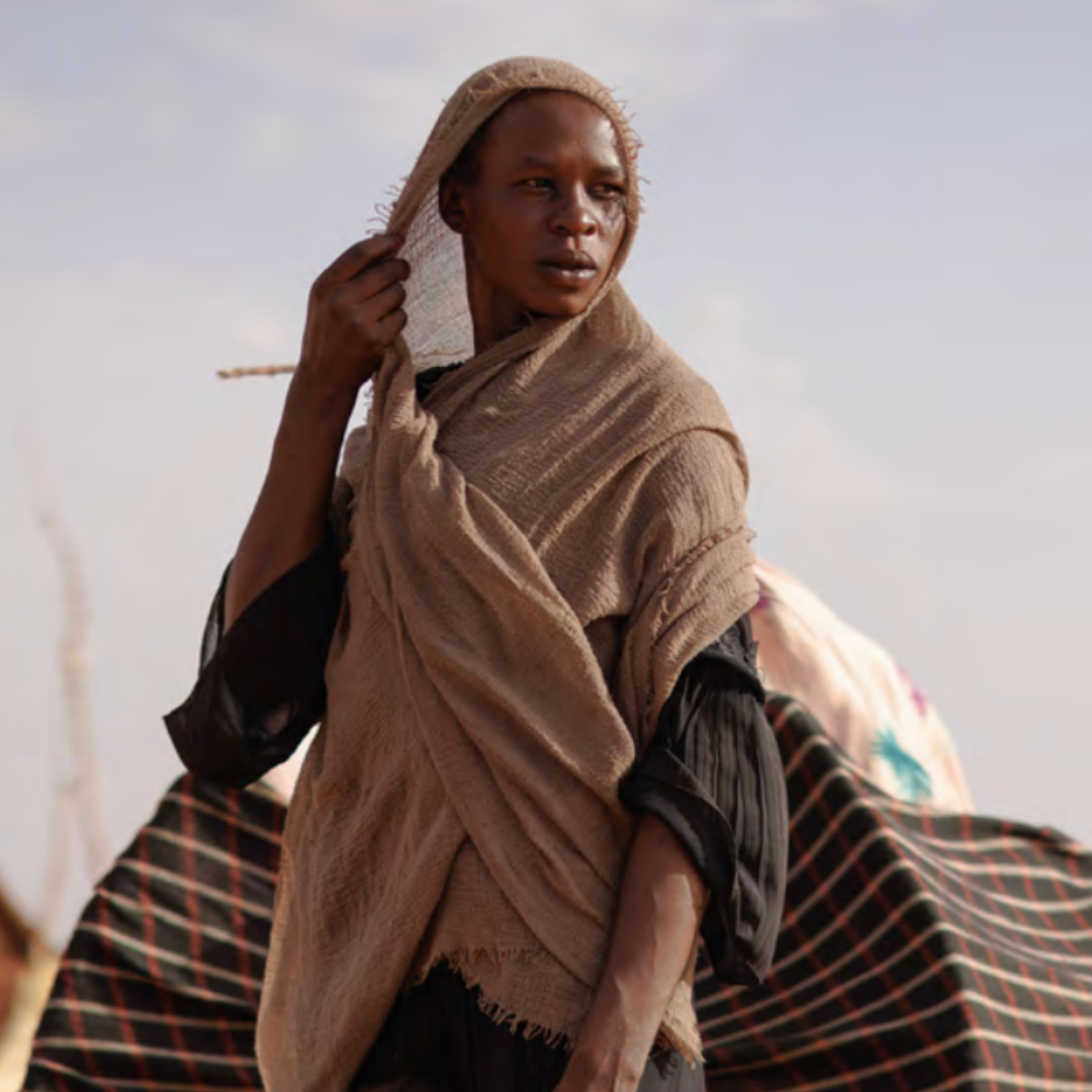 Femme dans un contexte humanitaire tenant un tissu sur la tête, illustrant la résilience des populations locales dans les crises humanitaires