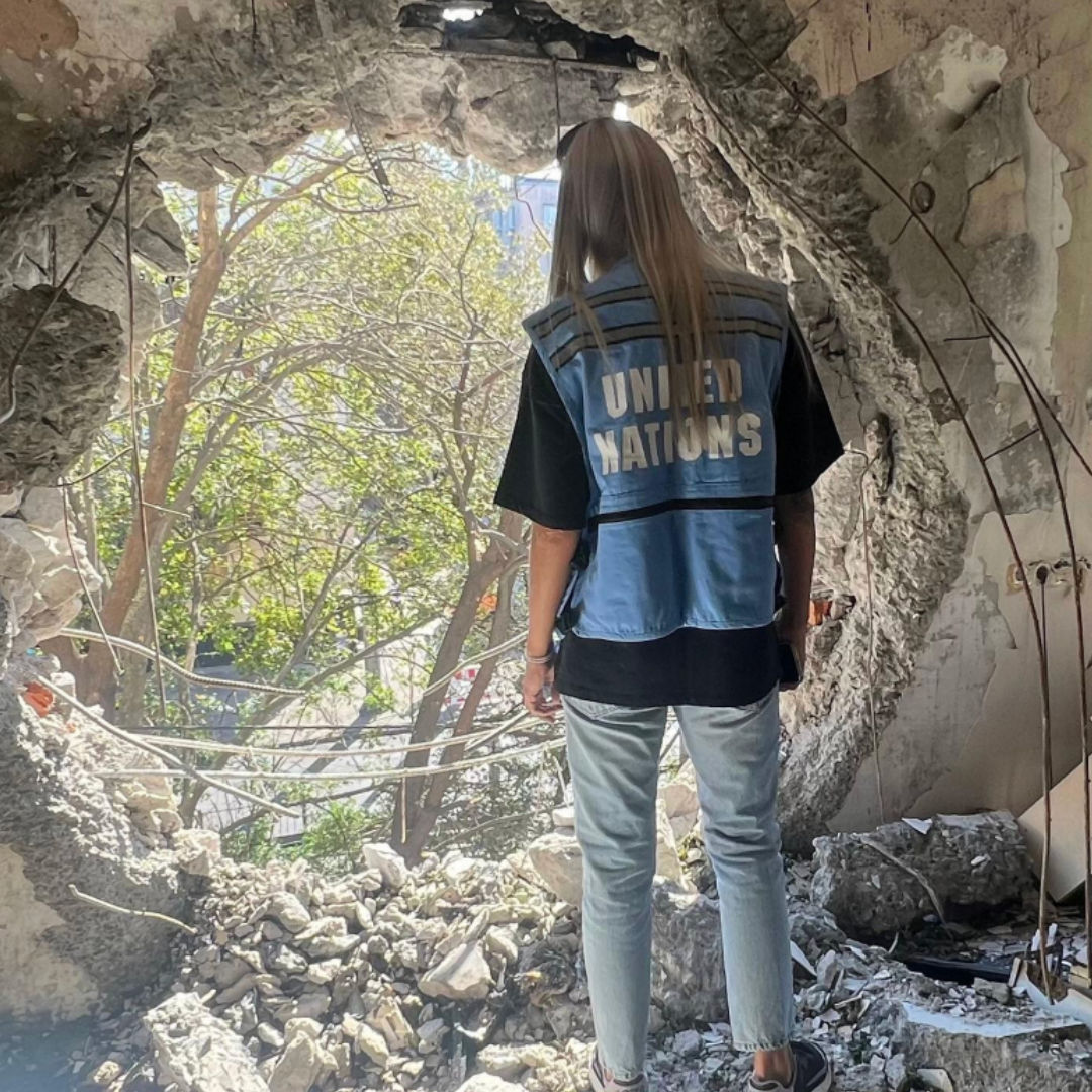 Travailleuse humanitaire des Nations Unies observant des dégâts dans un bâtiment détruit, illustrant la réalité des crises humanitaires et le travail de terrain des associations.